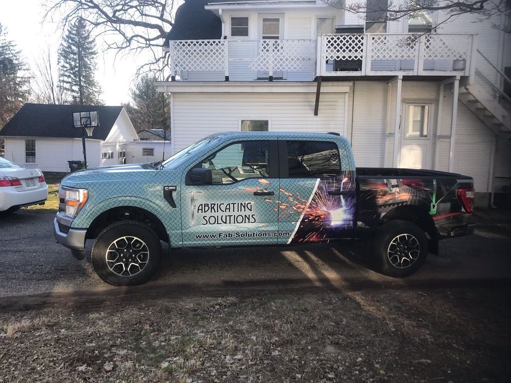 Wrapped black and teal pickup truck parked in a driveway beside a house