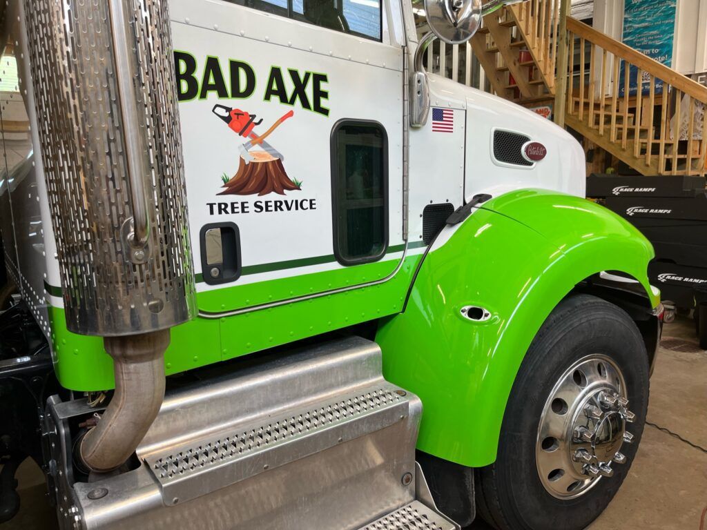 Bright green and white tree service truck with “BAD AXE” on the cab and a metal exhaust pipe.