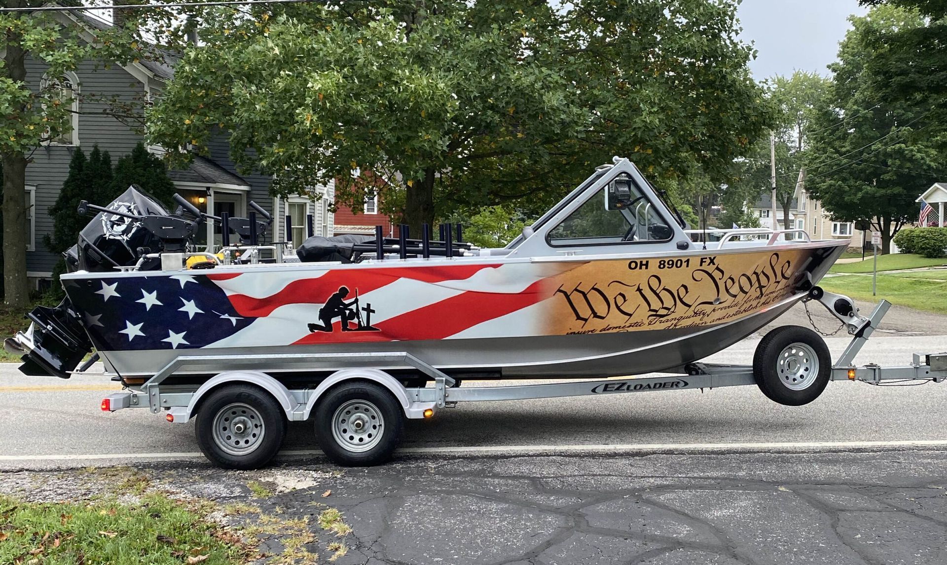 Patriotic-themed boat on a trailer parked on a street, with American flag and red, white, and blue graphics.