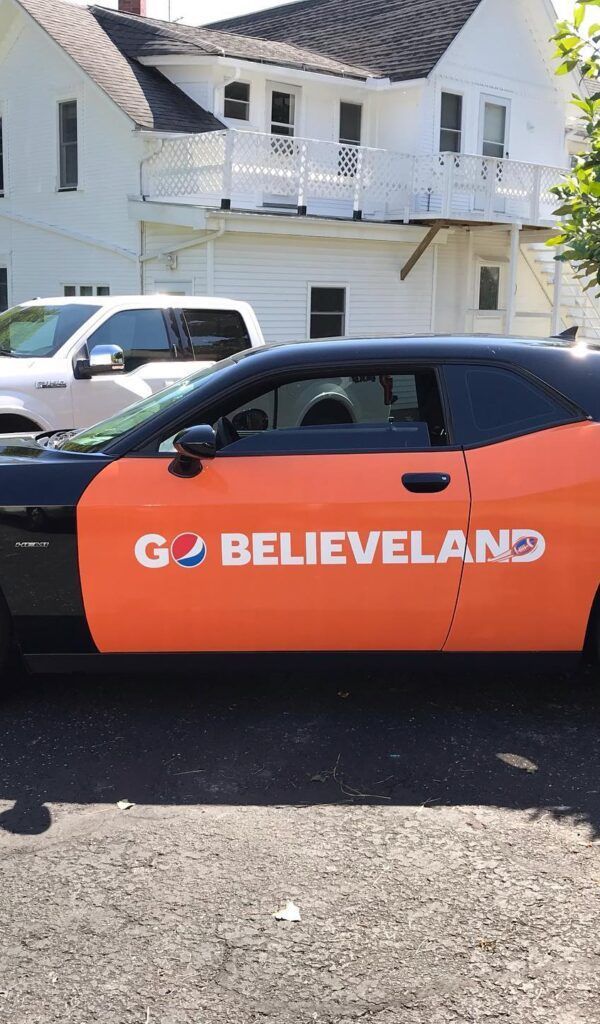 Orange-and-black GO BELIEVELAND car parked in front of a white building.
