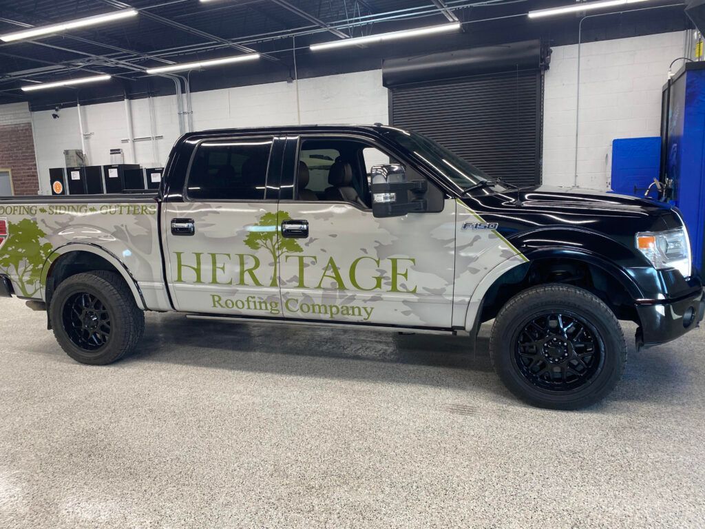 Heritage Roofing Company pickup truck parked indoors, black and silver wrap with logo