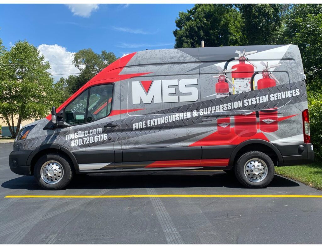 Gray MES service van with red graphics parked on a sunny street under a blue sky