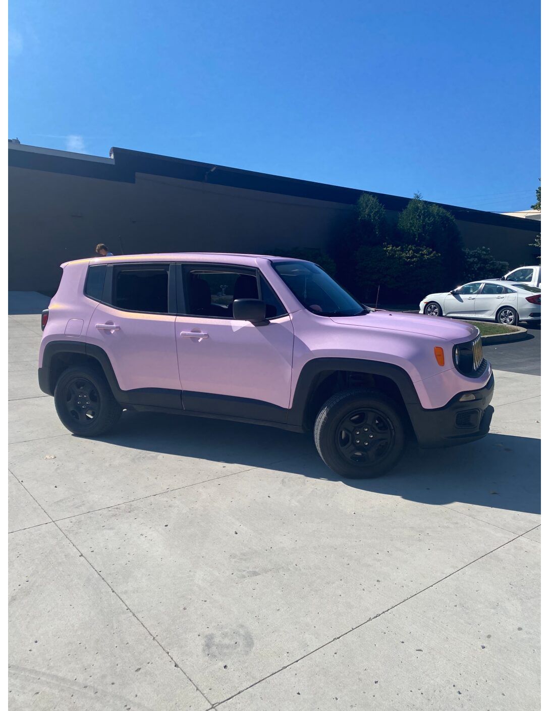 Light pink compact SUV parked in a sunny lot beside a dark building.