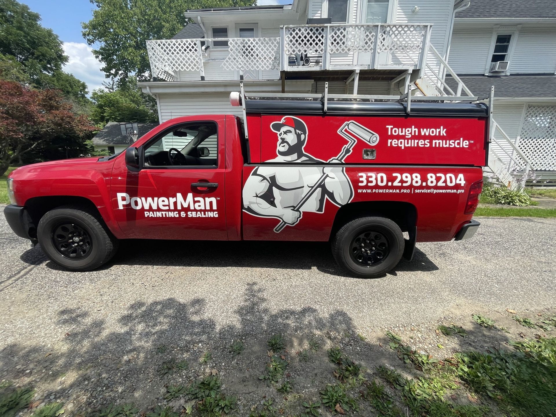 Red PowerMan service truck parked in a driveway beside a house, with a worker graphic and phone number on the side.