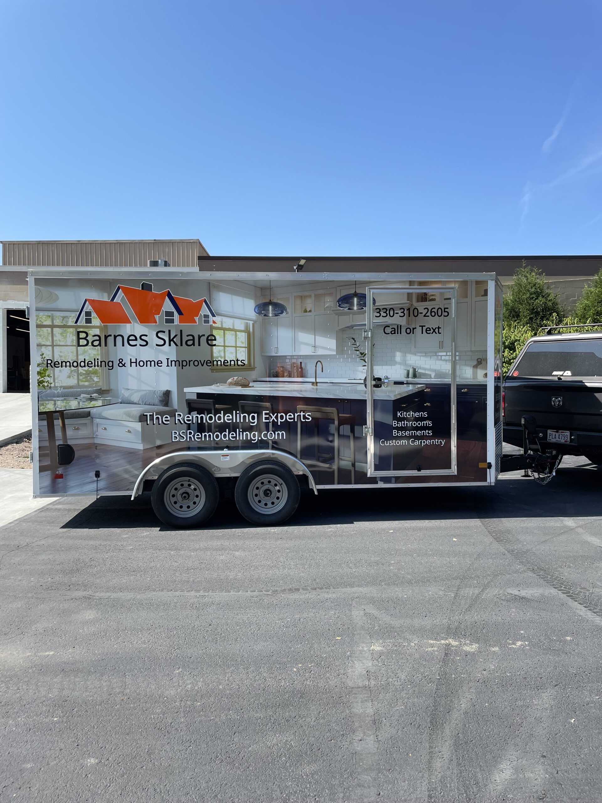 White enclosed utility trailer with company graphics parked in a lot under a clear blue sky.