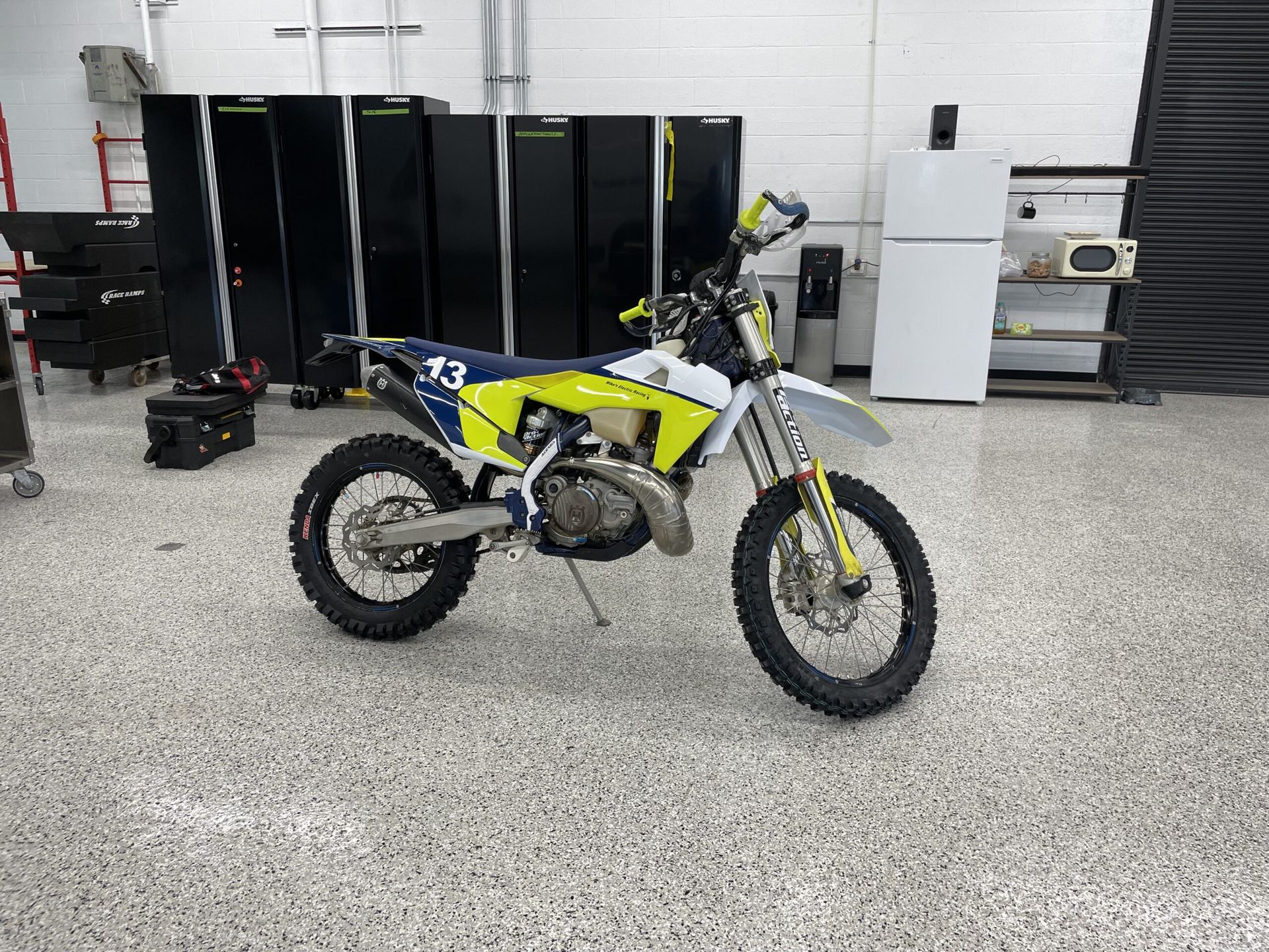 Yellow dirt bike in a garage workshop with black tool cabinets in the background