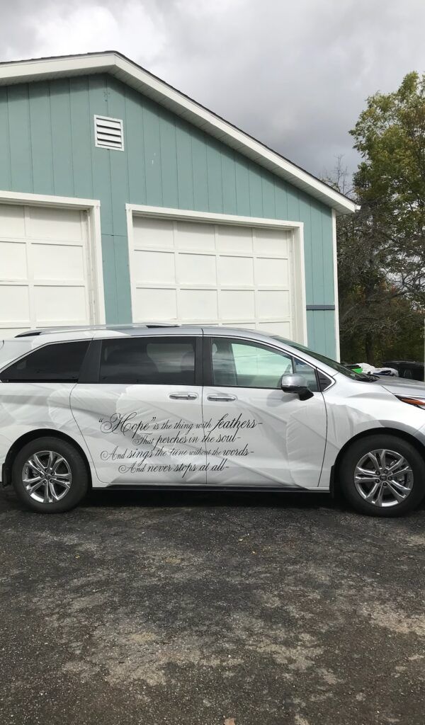 White minivan with black graphics parked in front of a light blue garage on a wet driveway