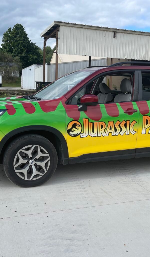 Colorfully painted SUV with Jurassic Park-style dinosaur graphics parked outdoors near a building