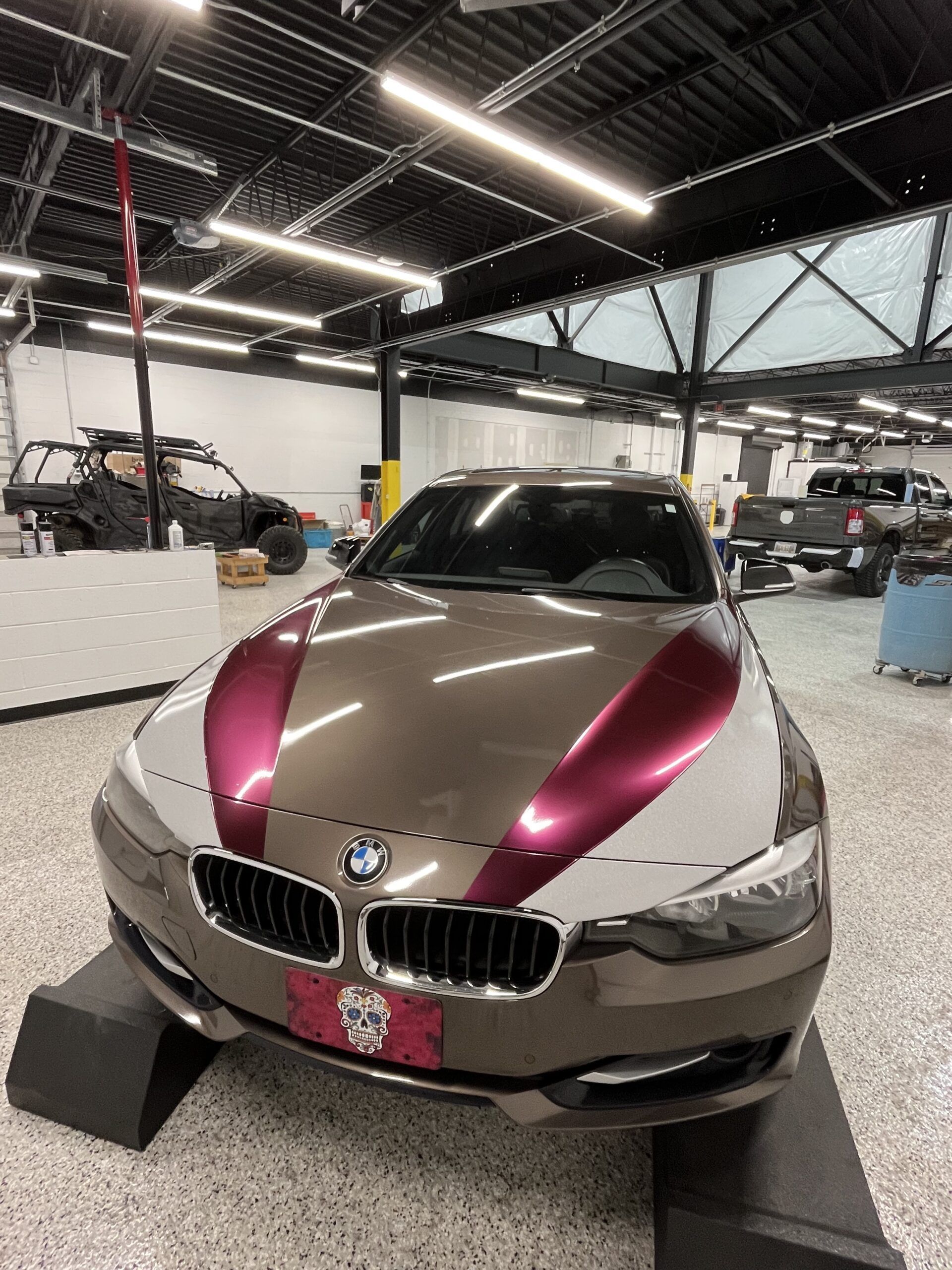Gold BMW with magenta hood accents displayed in an indoor showroom or garage.