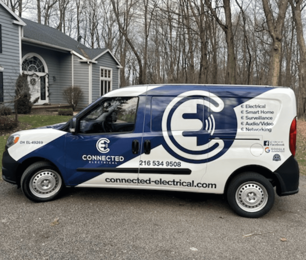 White and blue Connected Electrical service van parked outside a house with bare trees behind it