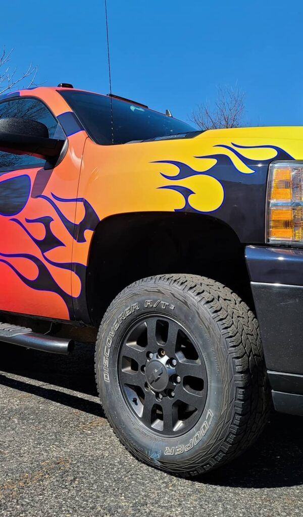 Custom black pickup truck with orange and purple flame paint, shown in a side view on pavement.