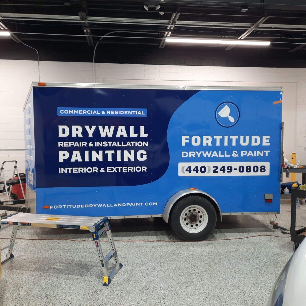 Blue drywall and painting service trailer in a garage, with “Fortitude Drywall & Paint” signage.