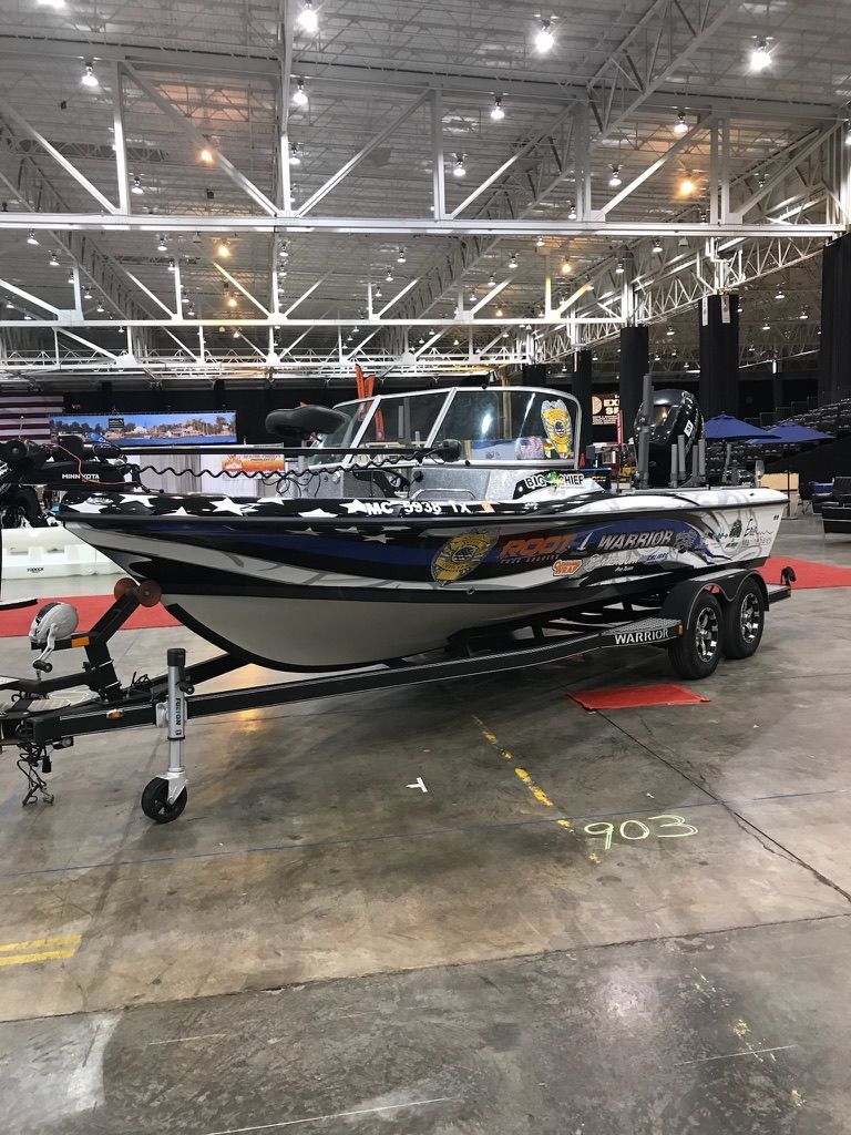 Black-and-white speedboat on a trailer inside a large convention hall under bright lights