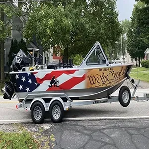 Small patriotic boat on a trailer with stars, stripes, and “We the People” lettering on a street.
