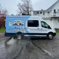 White mobile dog grooming van parked in a wet driveway, with blue branding and phone number 216-808-3056