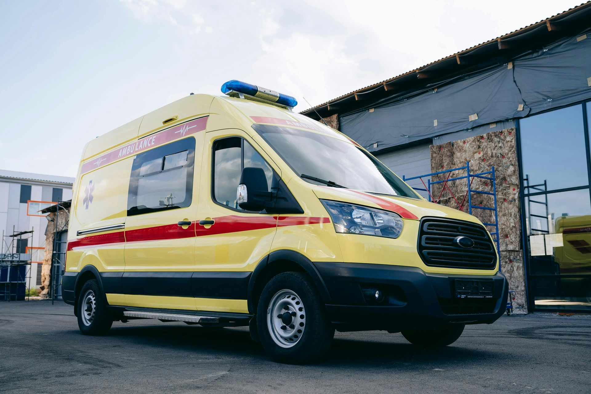 Yellow and red ambulance van parked beside an industrial building on a street