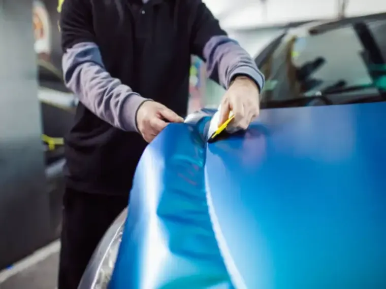 Person uses a red heat gun on a white car hood in a garage