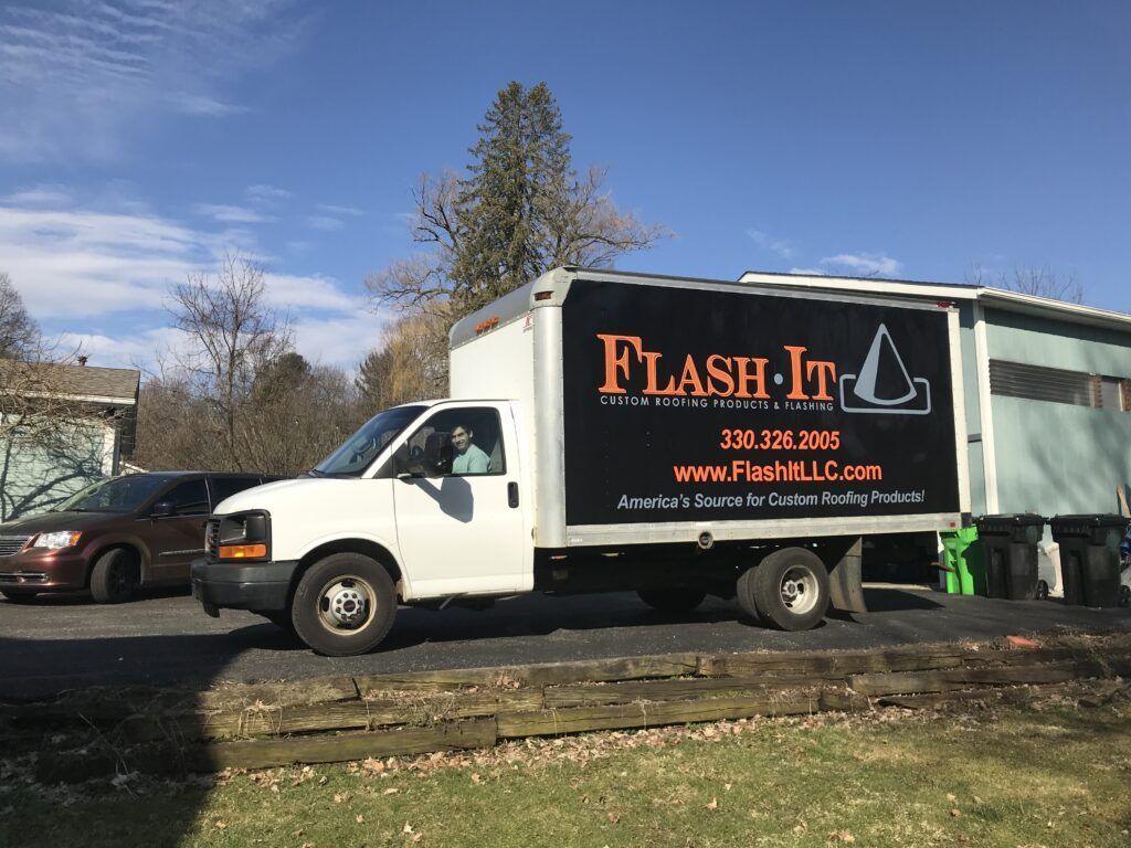 White Flash-It box truck parked outdoors by a road under a blue sky
