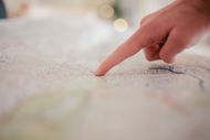 Hand holding a smartphone over a map with red location pins marking places