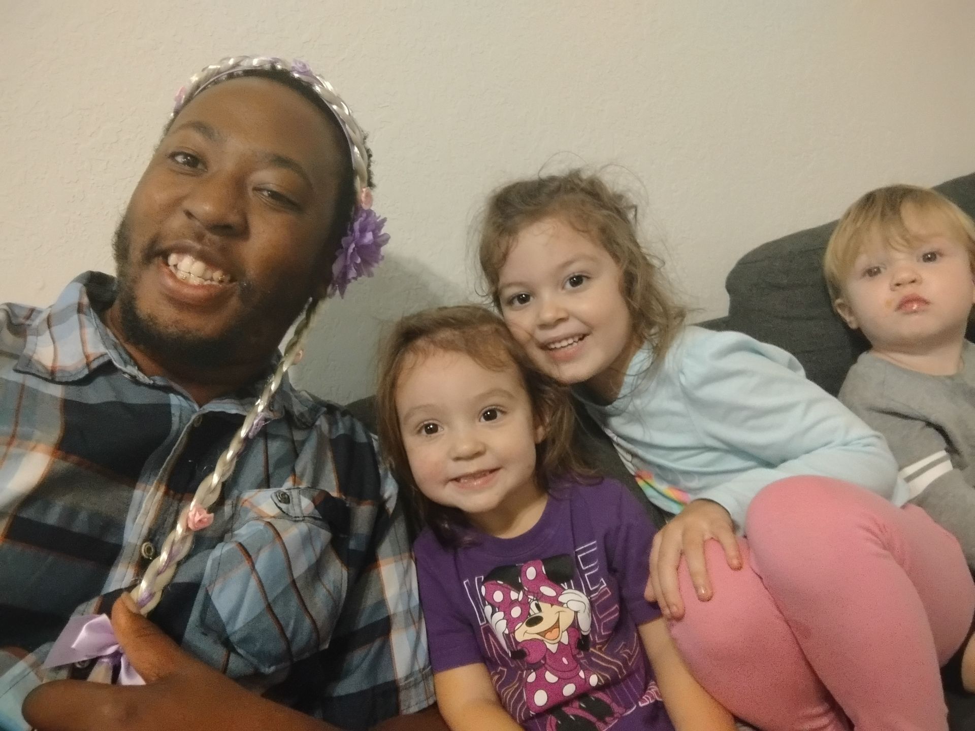 Man with a headband smiles with three young children on a couch.