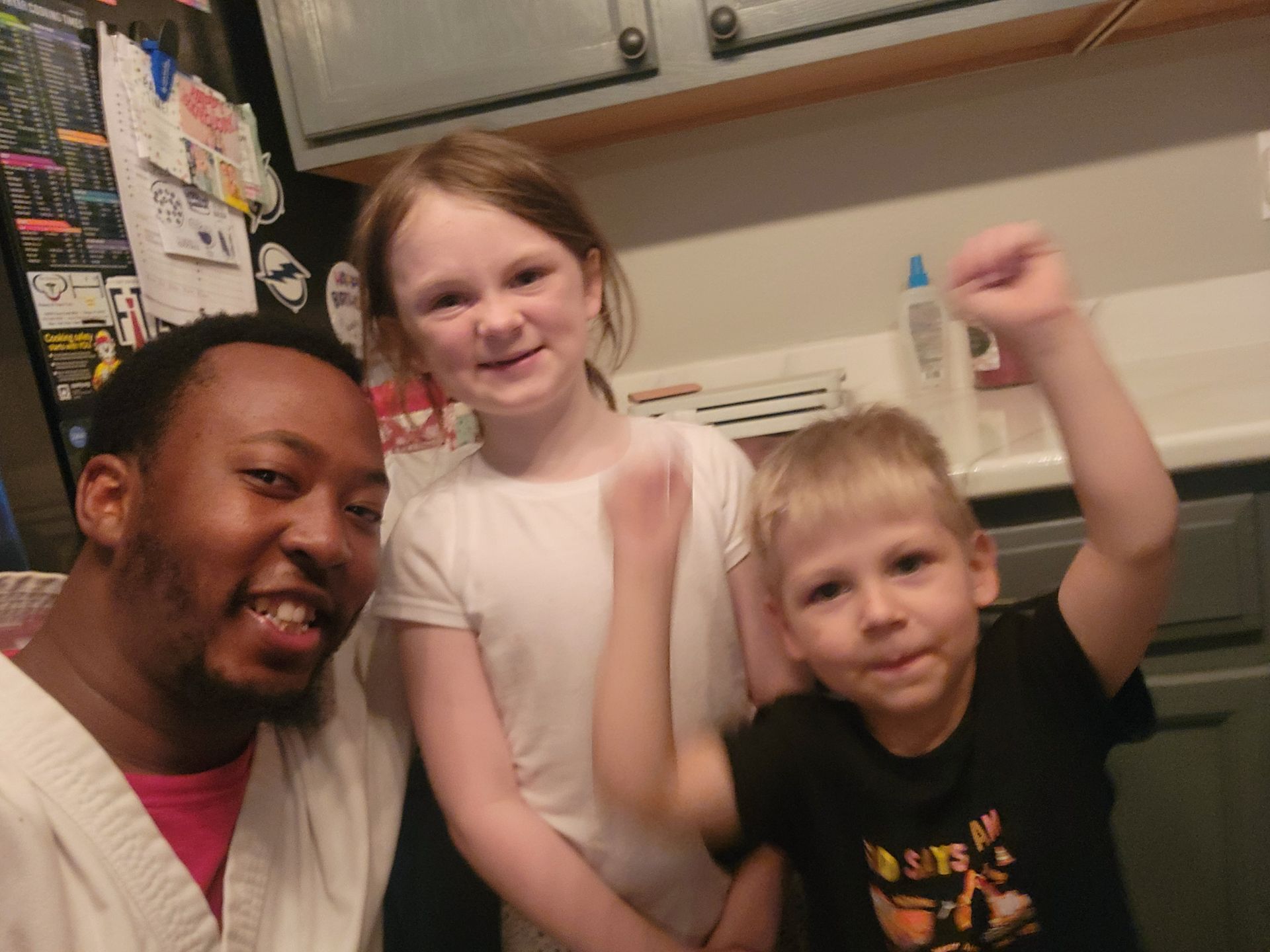 Man, and two kids smile. The boy raises a fist. They are in a kitchen.