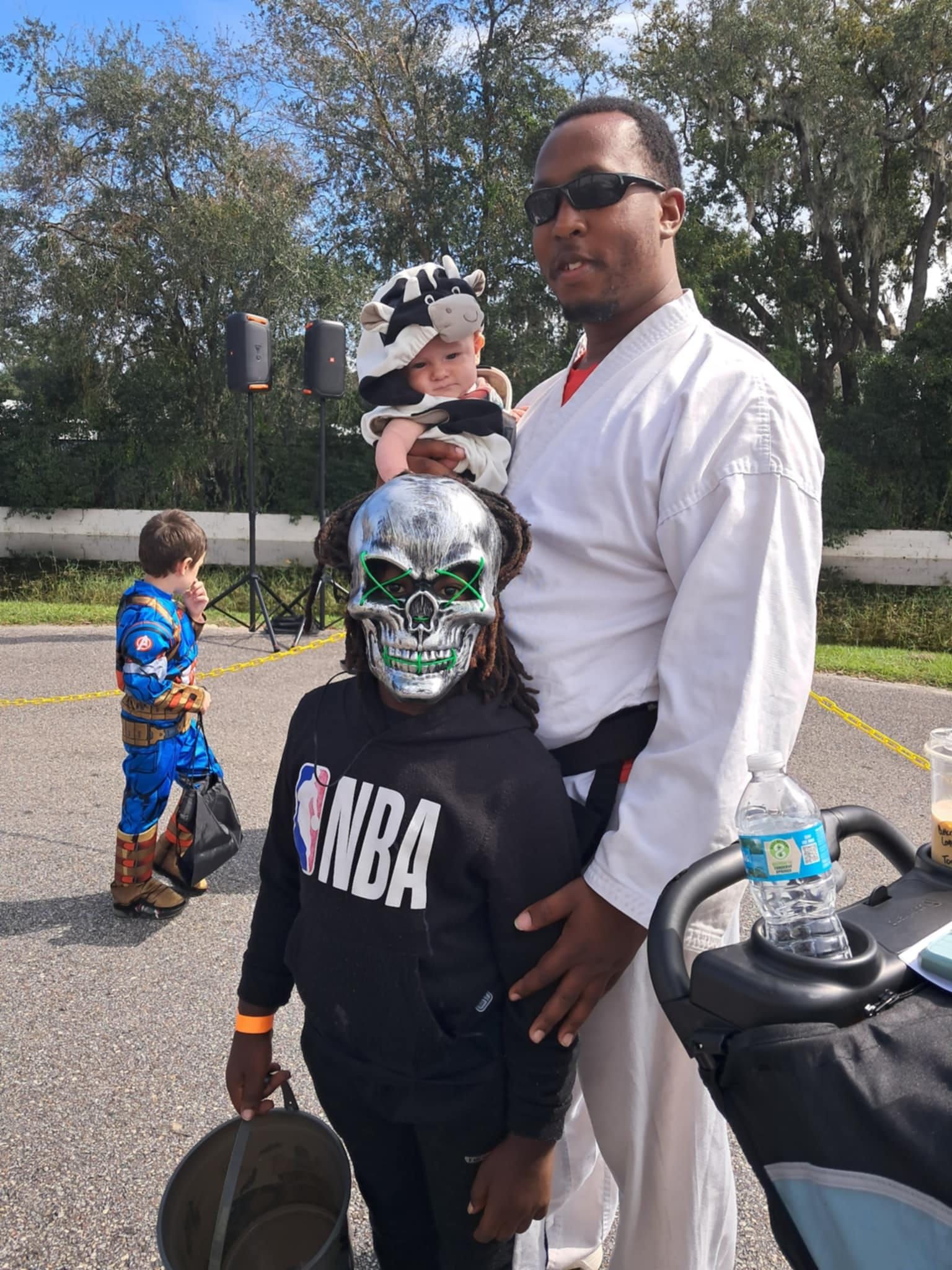 A man is holding a child in a stroller while wearing a skull mask.