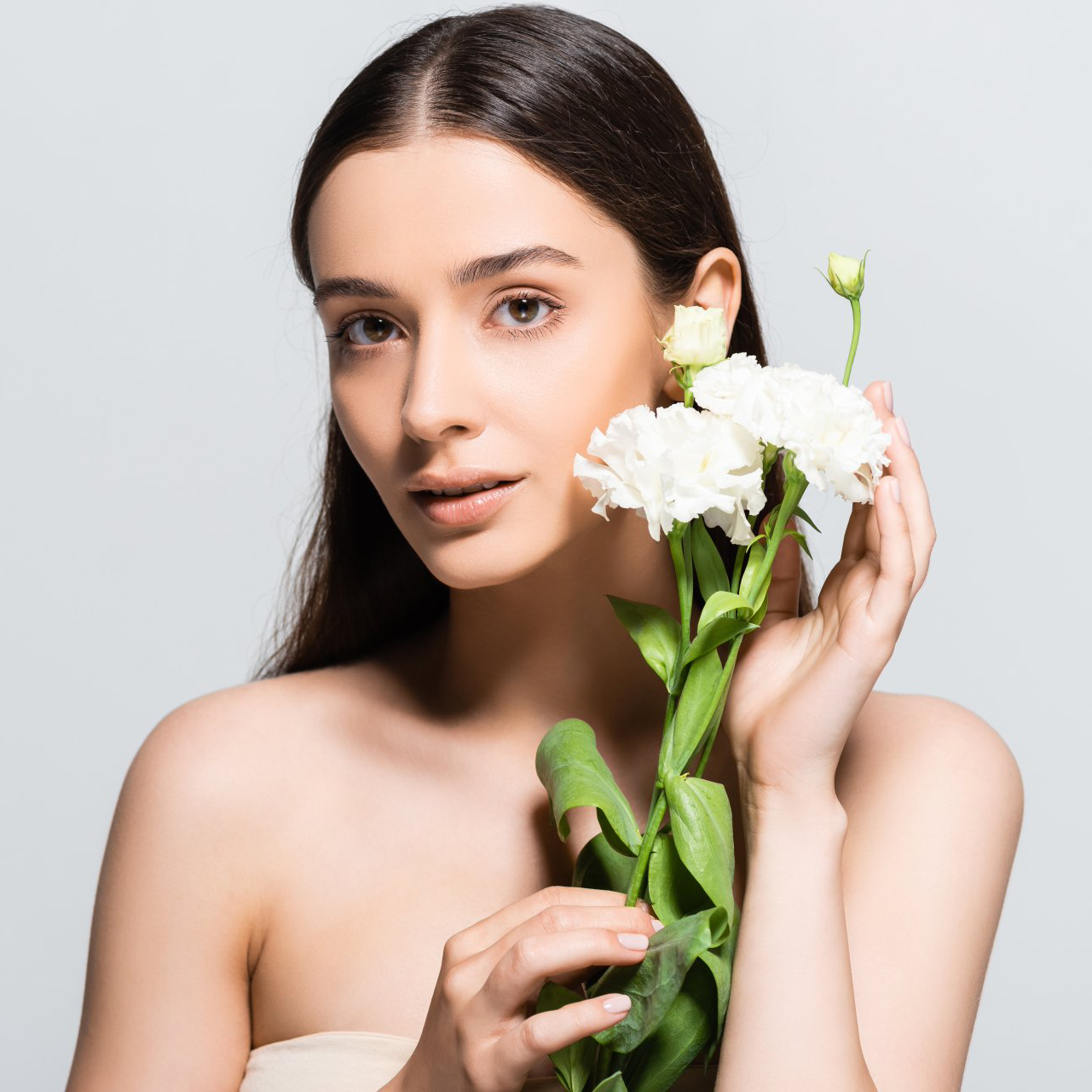 Woman holding white flowers, neutral expression, light skin, against a grey background.