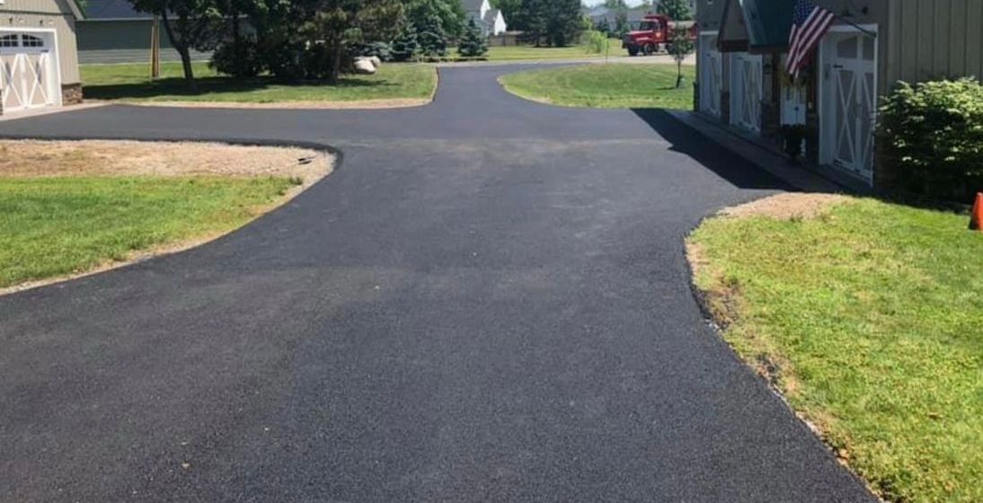 Close-up of an asphalt driveway edge finished by Universal Paving & Concrete in Rochester, NY, offering a neat and smooth transition to the lawn.