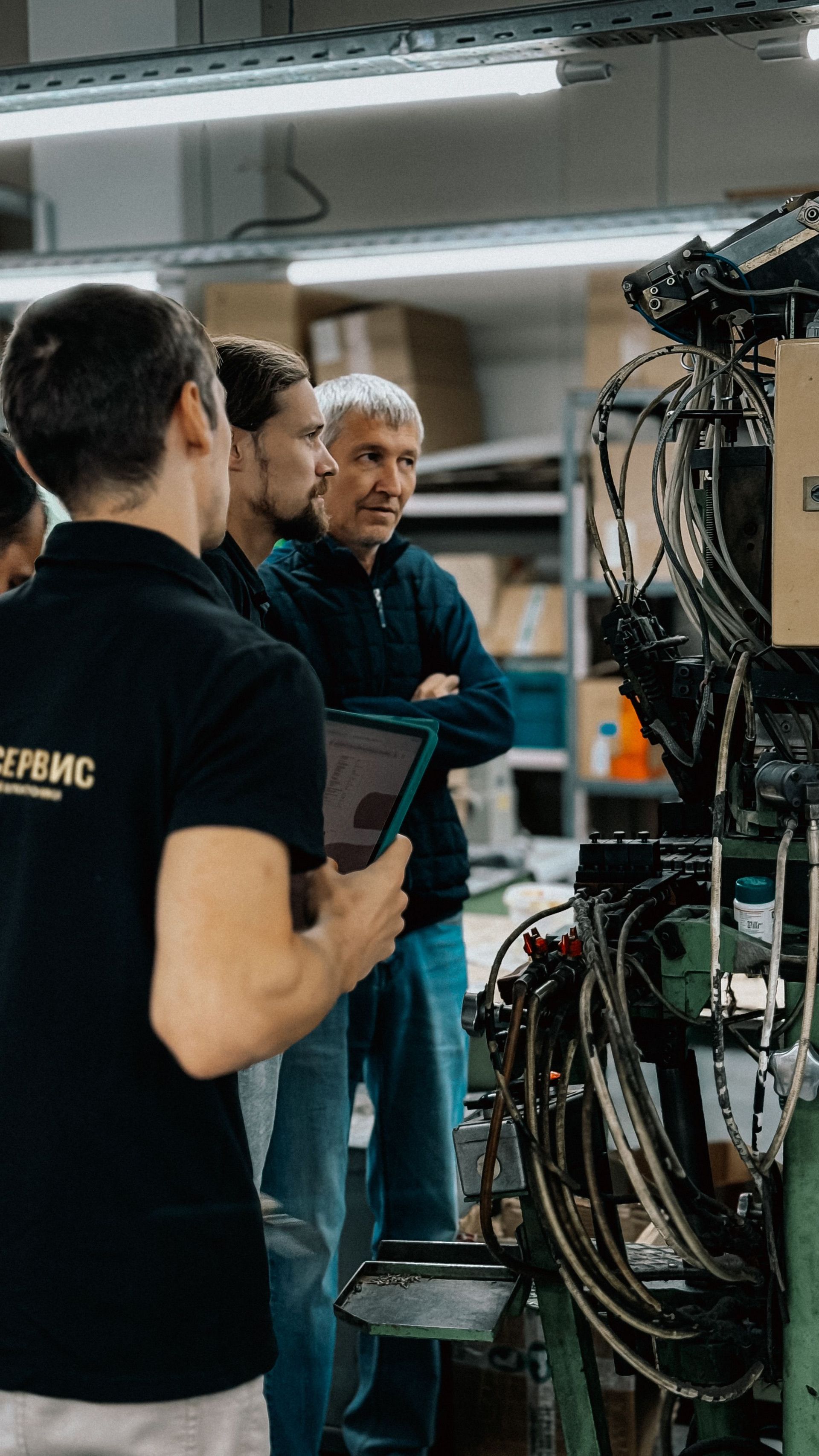 Three people inspecting tangled machinery and cables in a workshop