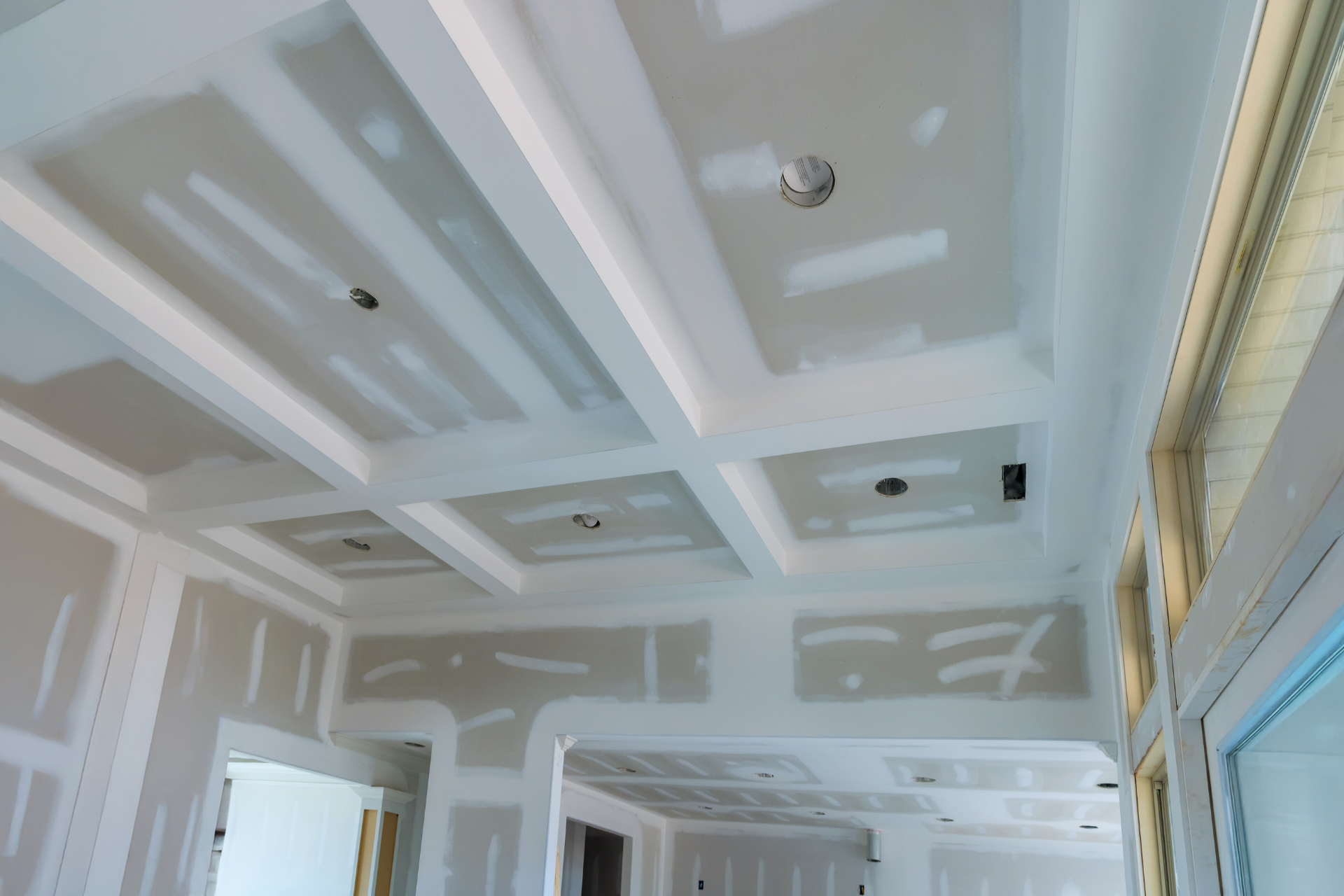 White room ceiling with recessed panels and lights, showing drywall finishing in progress