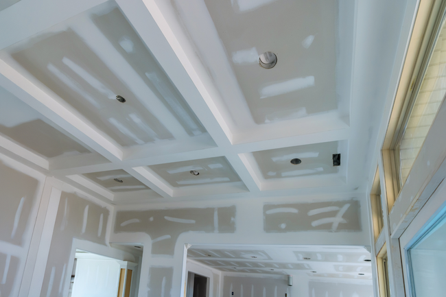 White room interior with unfinished ceiling drywall patches and tall windows on the right