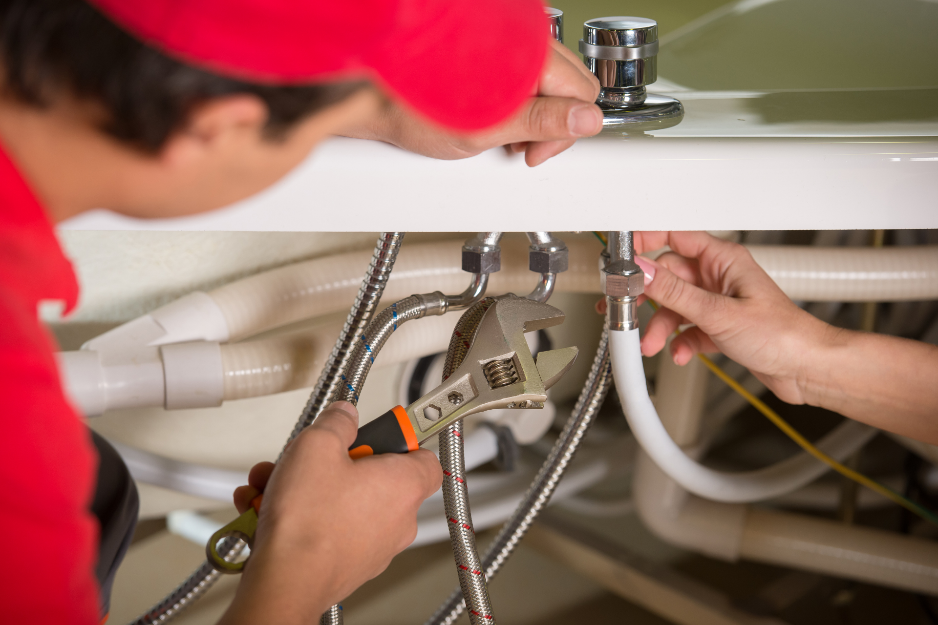 Plumber using wrench to repair sink pipes under a bathroom cabinet