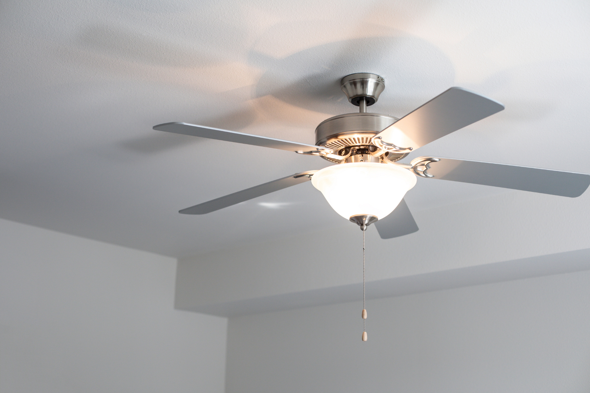 Ceiling fan with light fixture and pull chain on a white ceiling