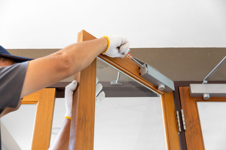 Person adjusting a metal door closer on a wooden door frame