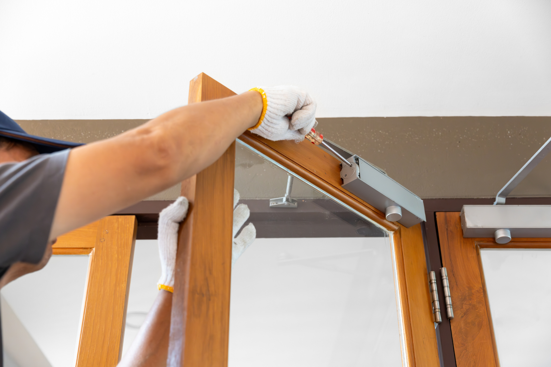 Technician installing a door closer on a wooden interior door frame