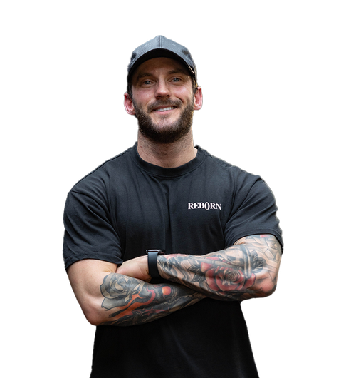 A man with a beard and tattoos is wearing a black shirt that says reborn