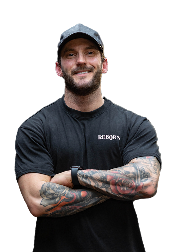A man with a beard and tattoos is standing with his arms crossed.