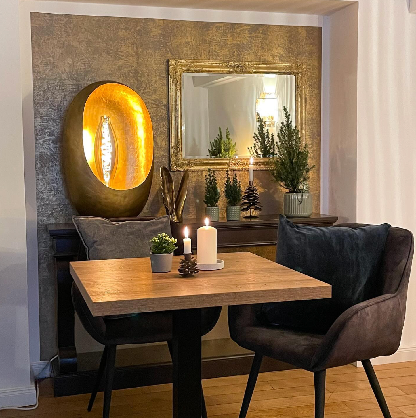 Gemütliche Restaurantecke mit Kerzenlicht am Tisch, dunklen Stühlen, Spiegel, Pflanzen und warmen Wandbildern.
