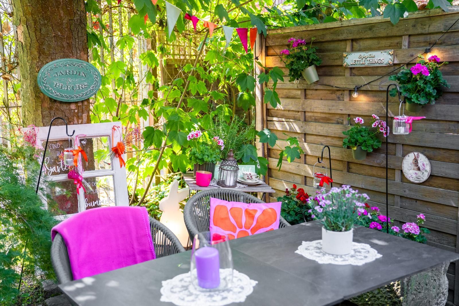 Farbenfrohe Gartenterrasse mit Tisch, Stühlen, Blumen und hängenden Pflanzen