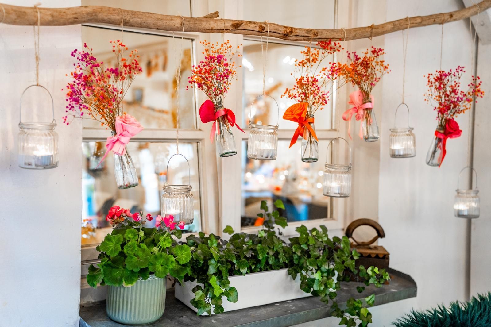 Dekorative Innendekoration mit hängenden Glaslaternen, rosa Blumen und einem üppig grünen Pflanzkübel auf einer Steintheke