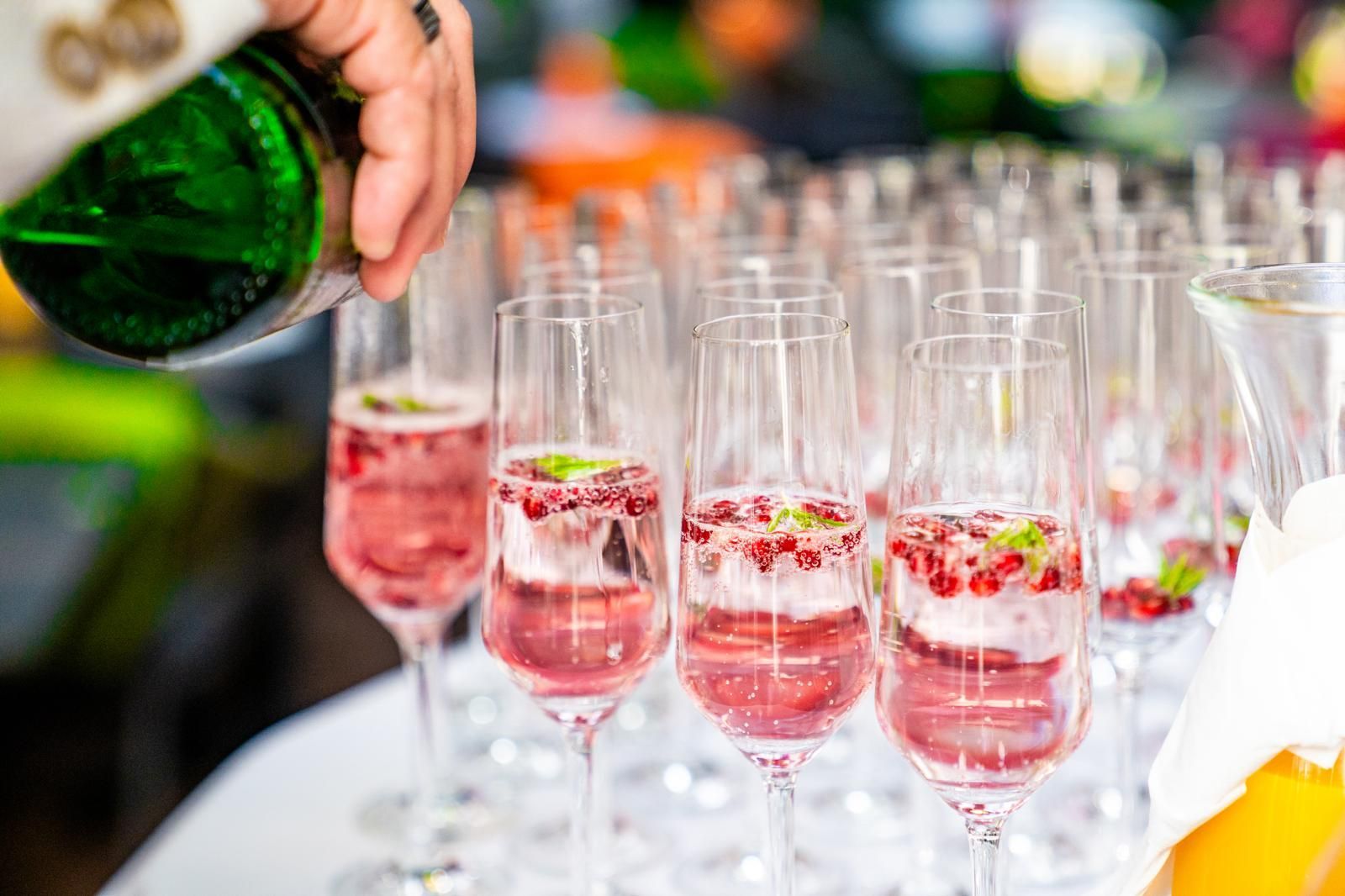 Bei einem Empfang wird Champagner in Reihen von rosafarbenen Sektgläsern mit Himbeeren eingeschenkt.
