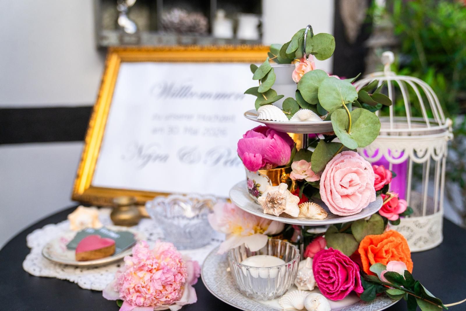 Dekorative Blumendekoration für eine Hochzeit mit rosa und orangefarbenen Rosen, einem gerahmten Schild und einem Vogelkäfig als Tischdekoration