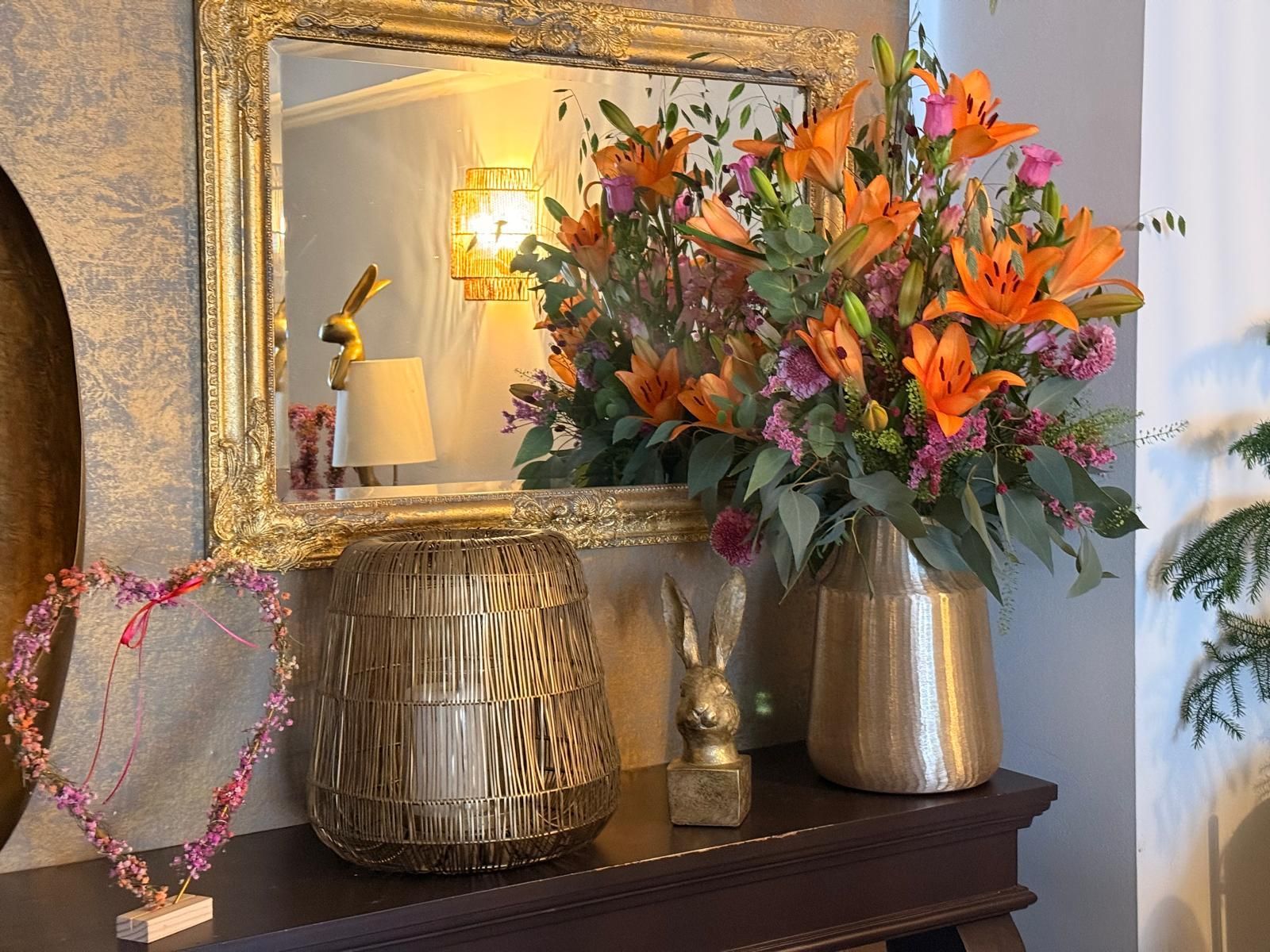 Dekorativer Kaminsims mit goldenem Spiegel, Vasen, rosa Herzgirlande und orangefarbenen Blumen