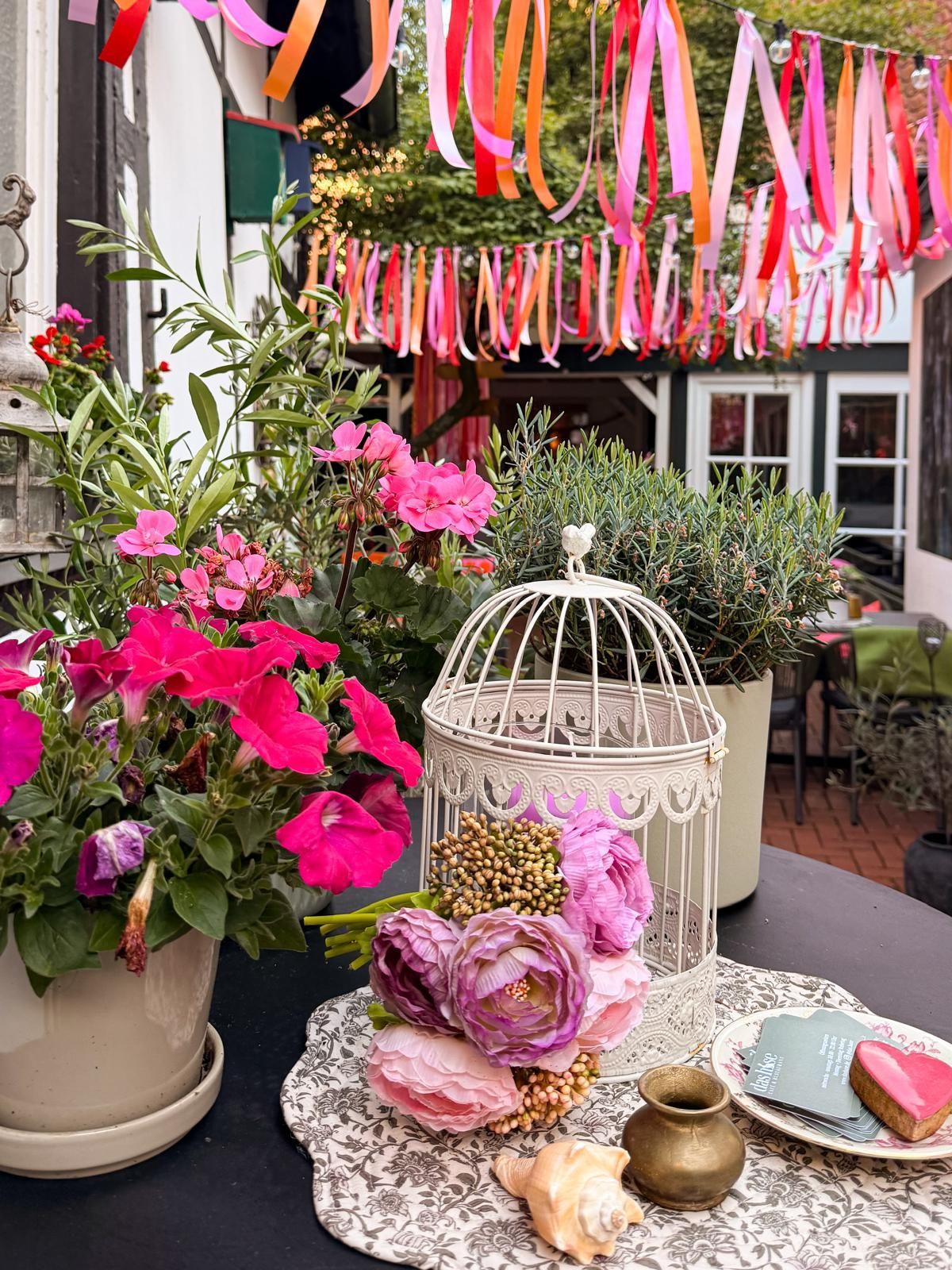 Ein mit rosa Blumen, Bändern und einem weißen Vogelkäfig als Mittelstück dekorierter Tisch im Freien