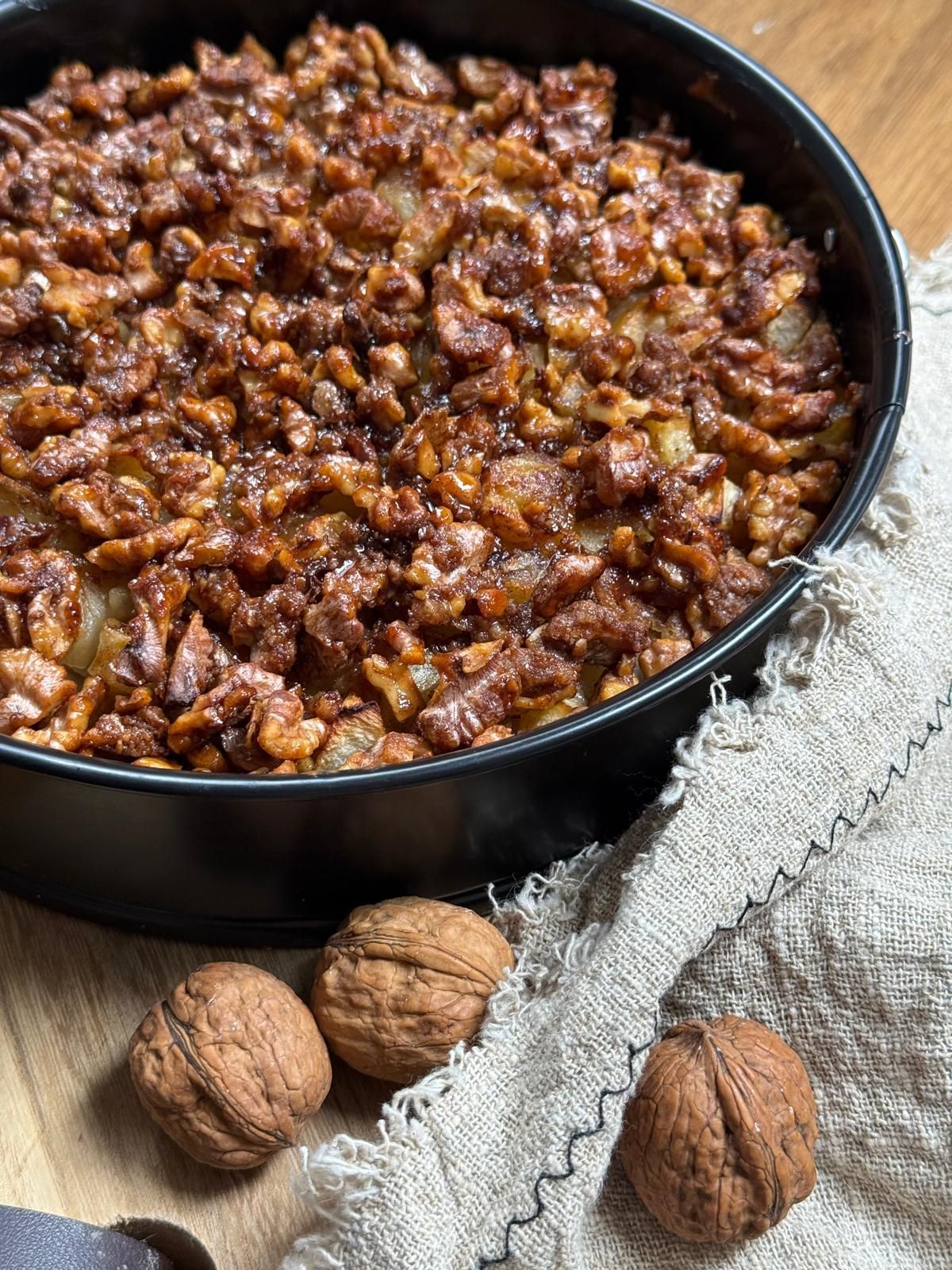 Eine Schüssel mit walnussbestreutem Dessert-Topping und ganzen Walnüssen auf einem grauen Tuch