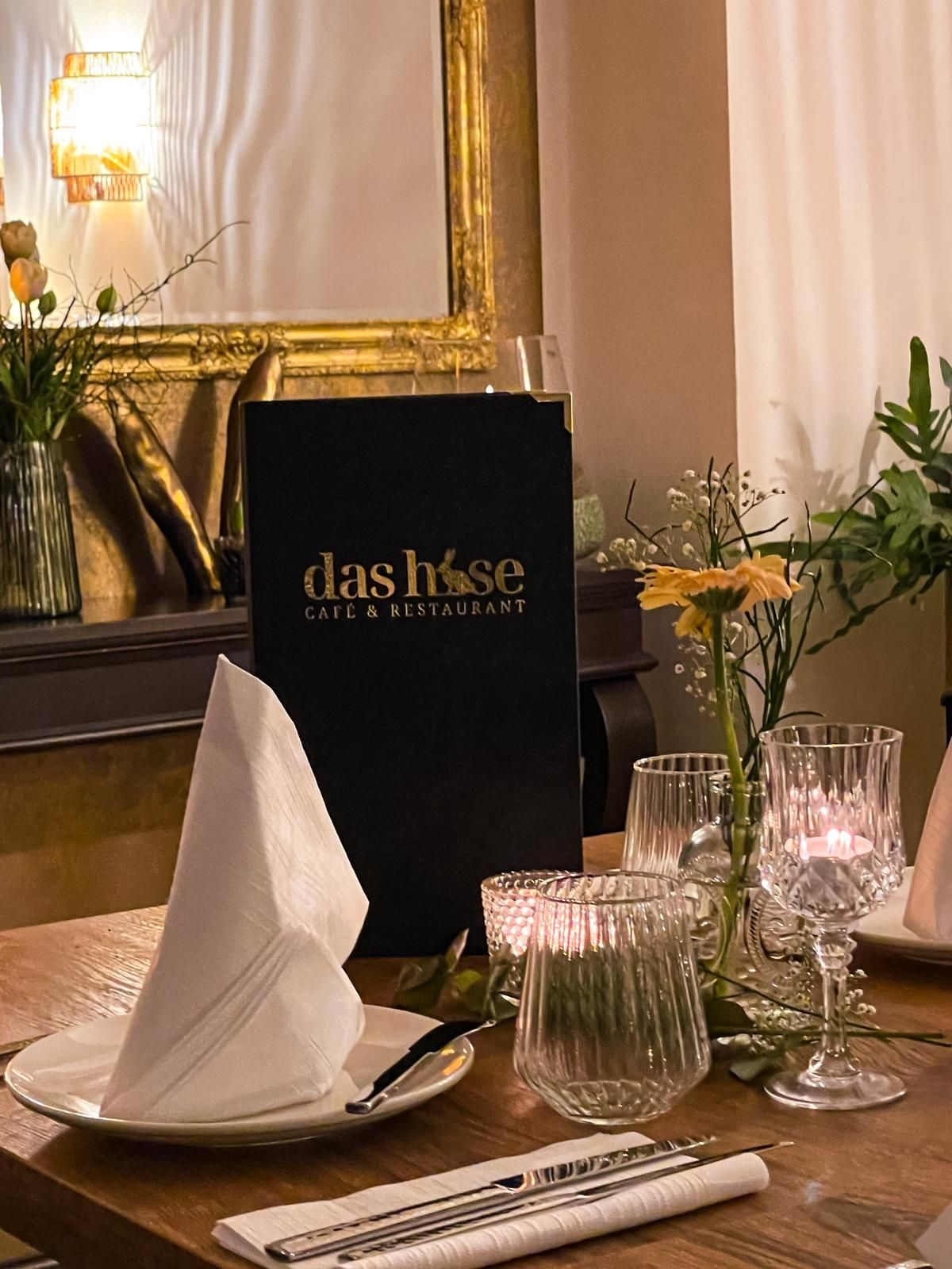 Elegant gedeckter Restauranttisch mit gefalteter Serviette, Gläsern und schwarzer Speisekarte an einem schwach beleuchteten Esstisch