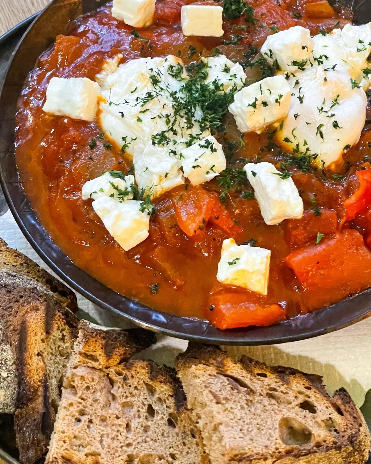 Eine Schüssel mit rotem Eintopf, überbacken mit Käse und Kräutern, serviert mit Scheiben knusprigem Brot.