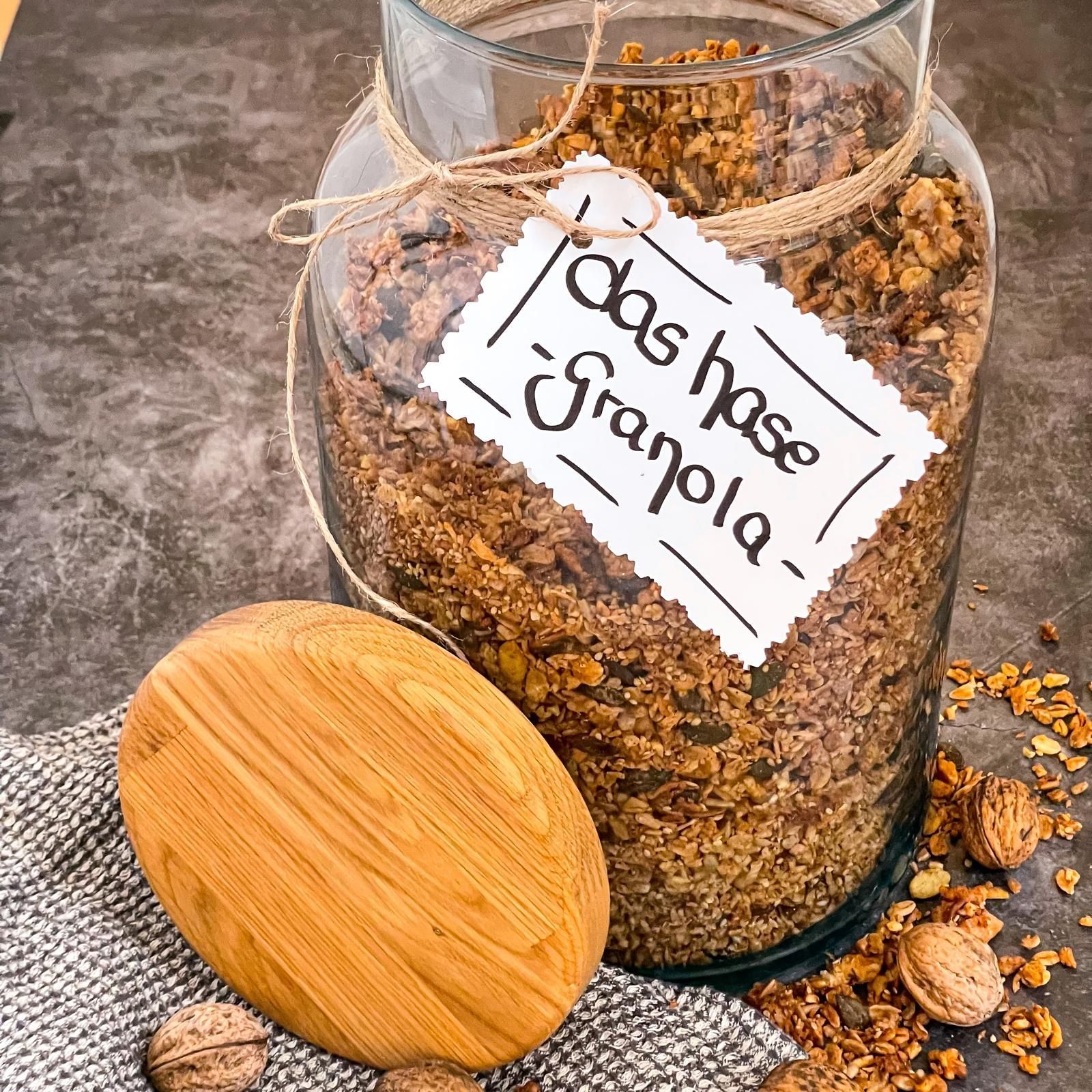 Ein Glas mit selbstgemachtem Müsli, handgeschriebenem Etikett und Holzdeckel auf einer Steinoberfläche