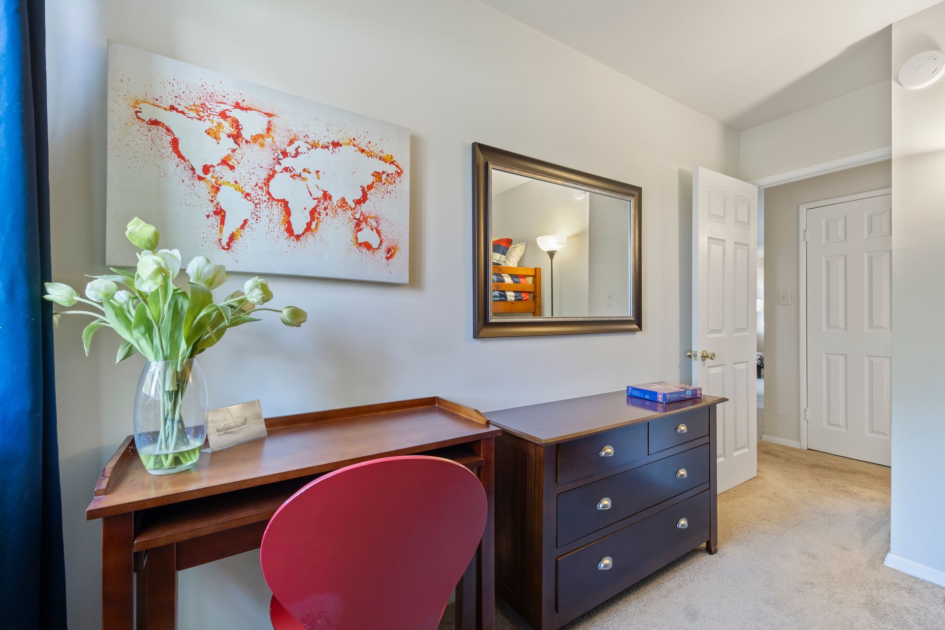 A bedroom with a desk , chair , dresser and mirror.