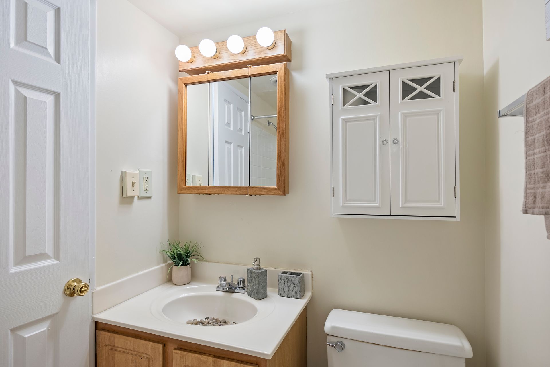 A bathroom with a sink , toilet , mirror and cabinets.